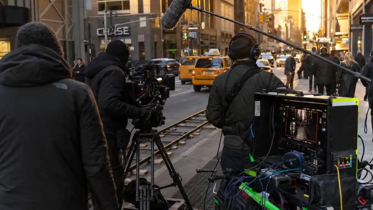 A real on-set film production scene in Manhattan with crew, camera and boom mic — the kind of working set Anne Hathaway and Conrad Ricamora shot Devil Wears Prada 2 scenes on before his role was cut