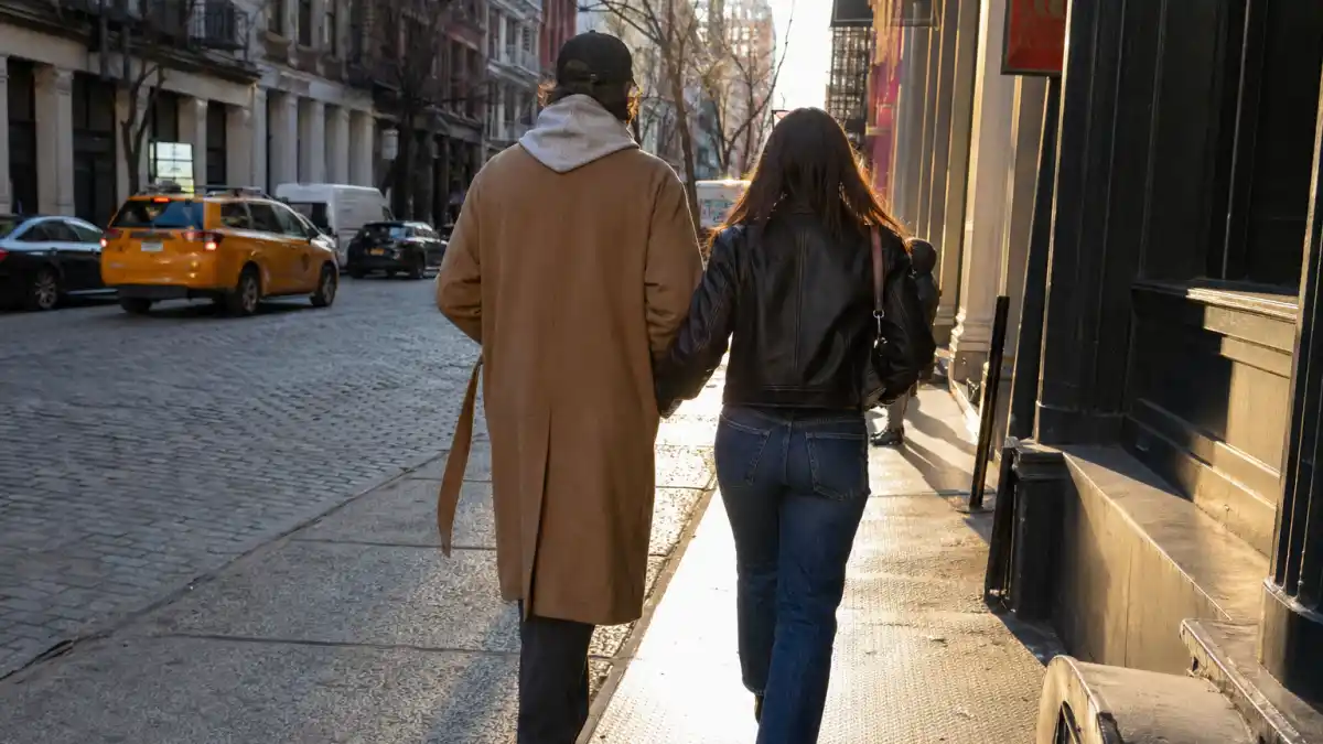Two people walking down a SoHo cobblestone street in New York City viewed from behind, in a candid paparazzi-style press photo — the kind of casual NYC walk Kelsea Ballerini and Chase Stokes were photographed taking
