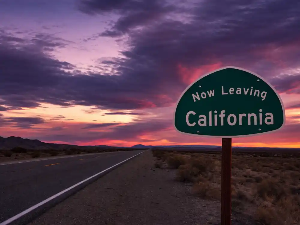 Now Leaving California highway sign at sunset symbolizing the migration of celebrities who left California