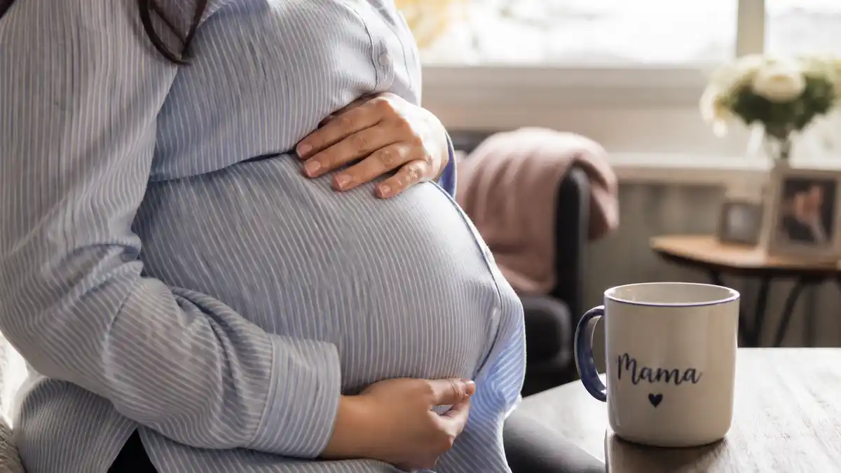 Natasha Bure pregnant announcement showing baby bump with matching Mama mug in cozy living room