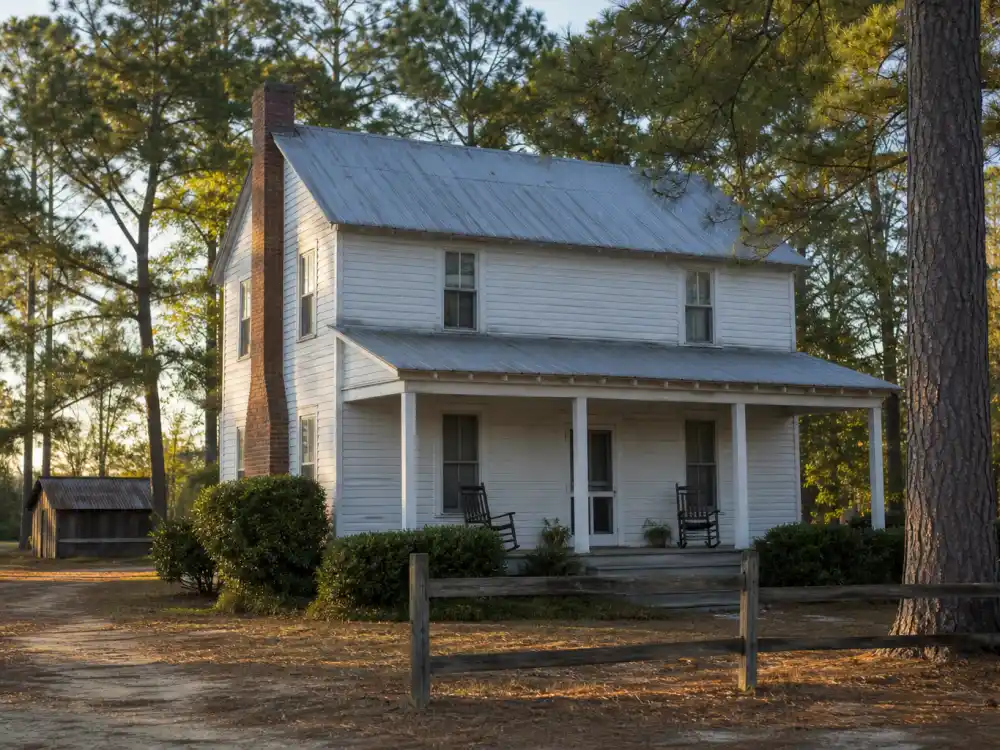Weathered wood-frame Mississippi farmhouse with tin roof and front porch — the celebrity childhood home where Oprah Winfrey grew up