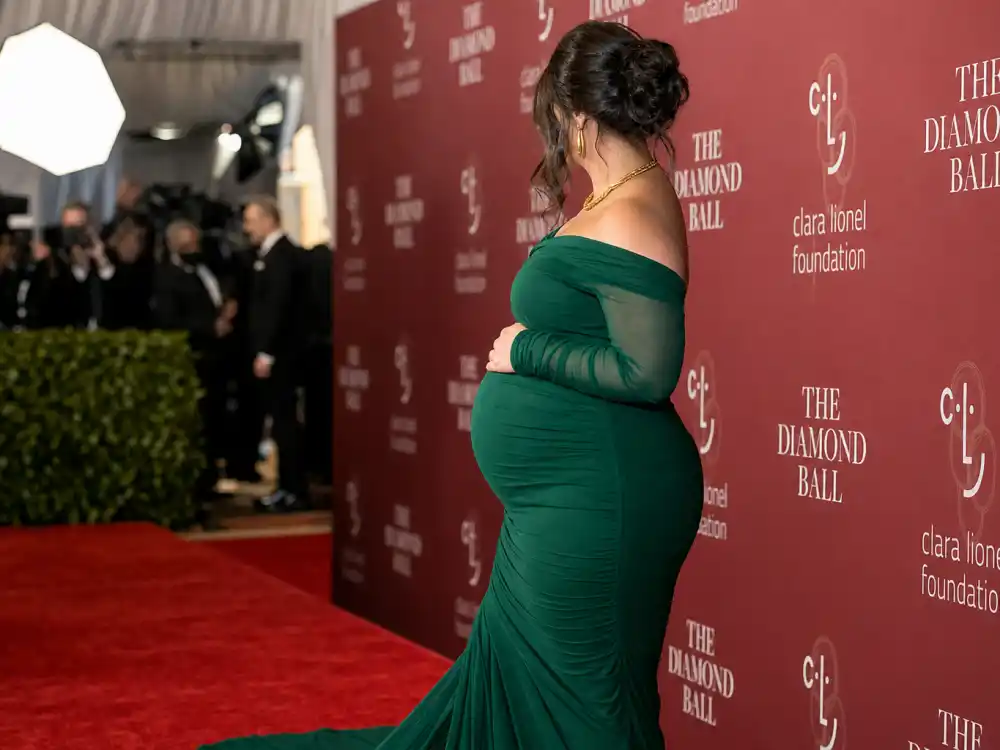 Anonymous plus-size pregnant woman in emerald green bodycon gown on red carpet for Ashley Graham maternity fashion guide formal event dressing