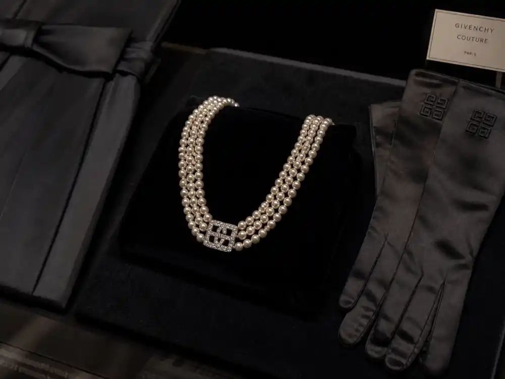 Multi-strand pearl necklace and black opera gloves beside little black dress fabric swatch amplifying Audrey Hepburn little black dress Givenchy accessory formula