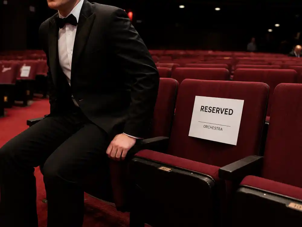 Anonymous guest in formal black attire sliding into a reserved orchestra seat — seat filler cooperation reflects award show etiquette rules celebrities follow when leaving rows