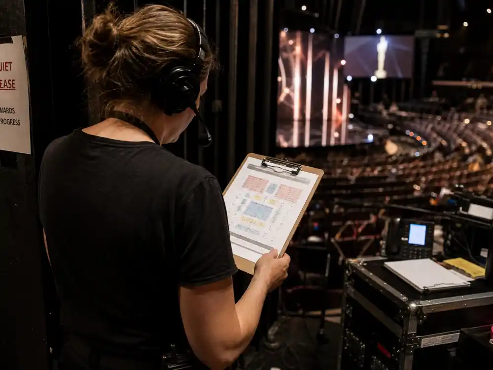 Stage manager with headset reviewing a seating chart in an empty awards theater — production logistics behind award show seat fillers explained