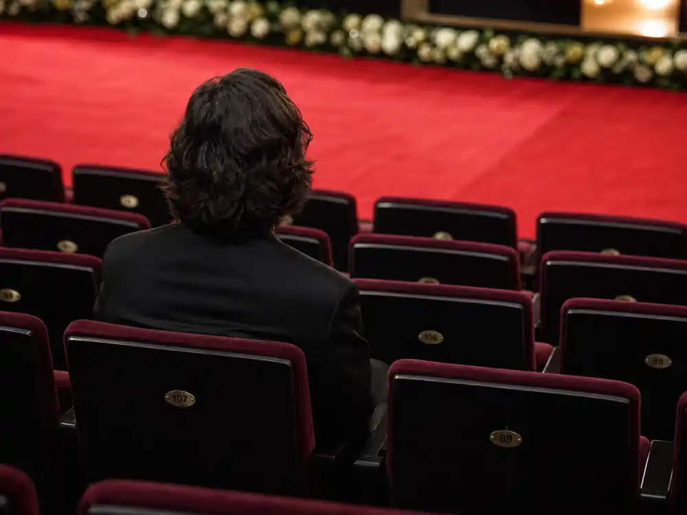 Anonymous seat filler in formal attire sitting alone in an empty award show theater seat — part of award show seat fillers explained