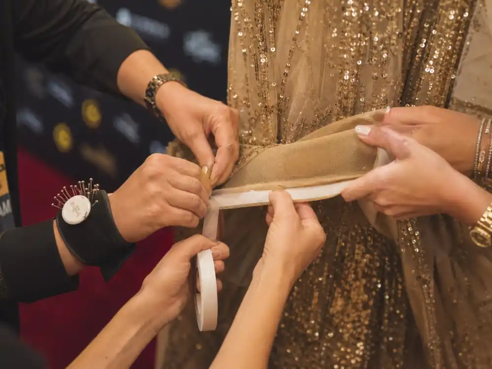 Stylist hands applying fashion tape to couture gown before awards show captures red-carpet prep that prevents award show wardrobe malfunctions live TV