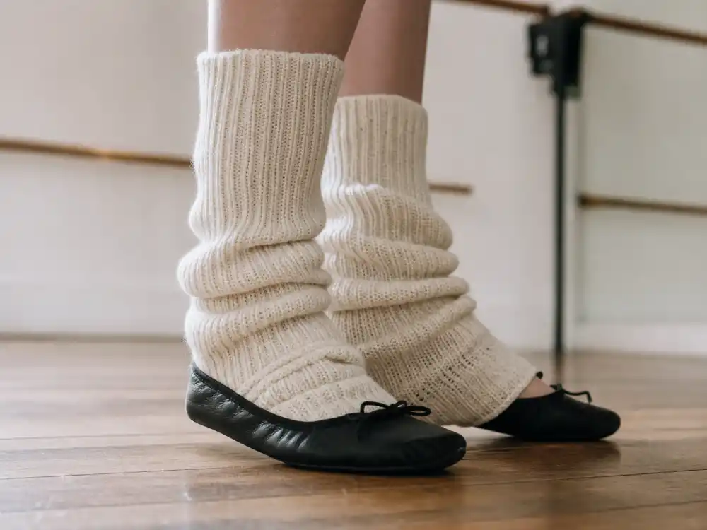 Cream ribbed leg warmers layered over black ballet flats at studio barre defining balletcore celebrity fashion trend legwear codes