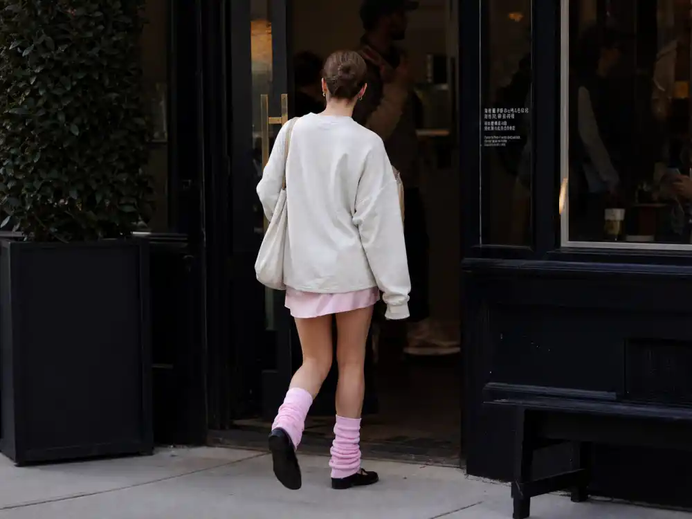Anonymous woman from behind in oversized cream sweatshirt pink leg warmers and black ballet flats exiting coffee shop for balletcore celebrity fashion trend sidewalk galleries