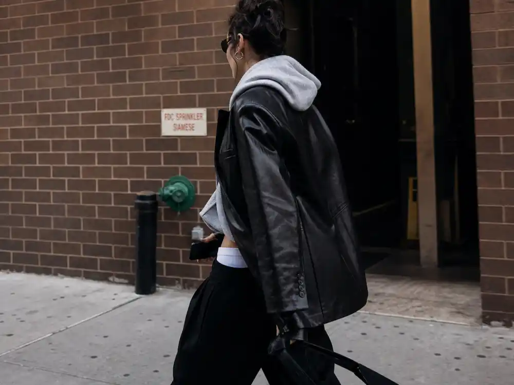 Oversized black leather blazer over hoodie defining Bella Hadid off duty street style layering contrast