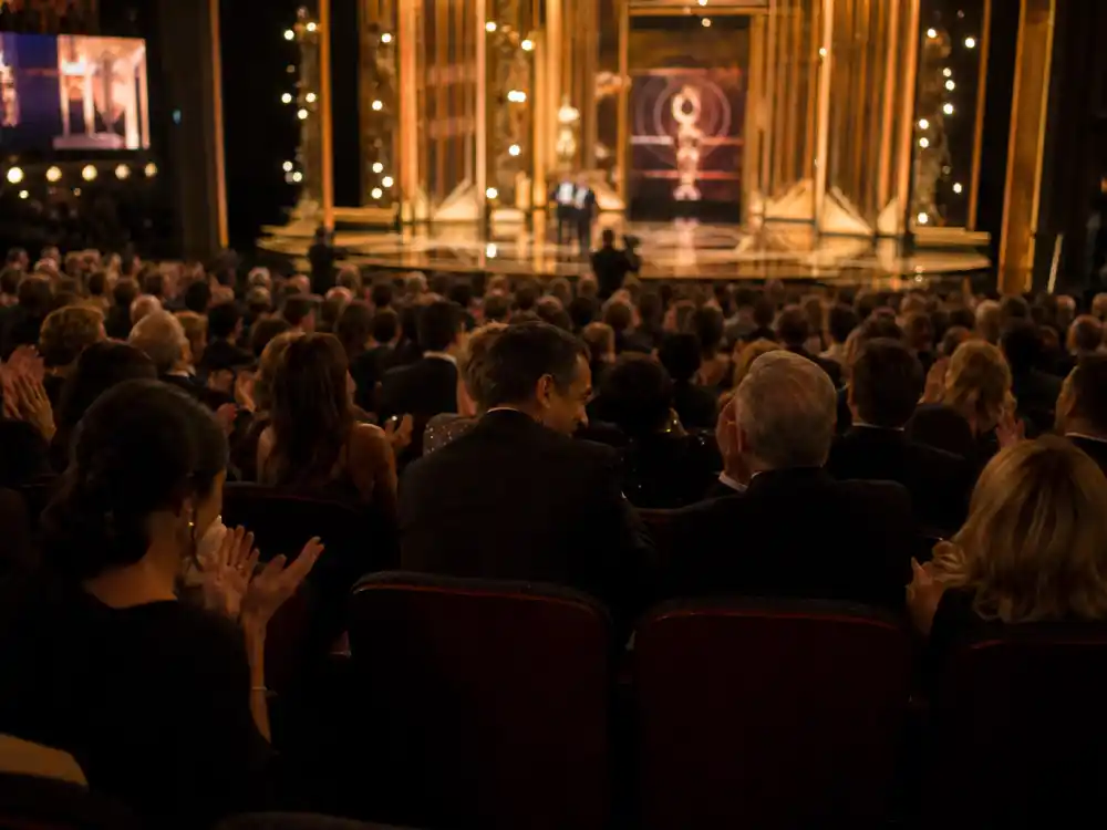 Laughing audience silhouettes react to monologue jokes from contenders among the best award show hosts of all time during a live ceremony broadcast