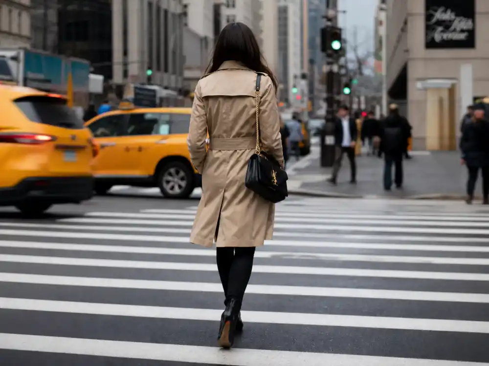 Anonymous woman from behind crossing Manhattan crosswalk in camel trench coat and designer handbag for best celebrity street style of all time NYC paparazzi moment