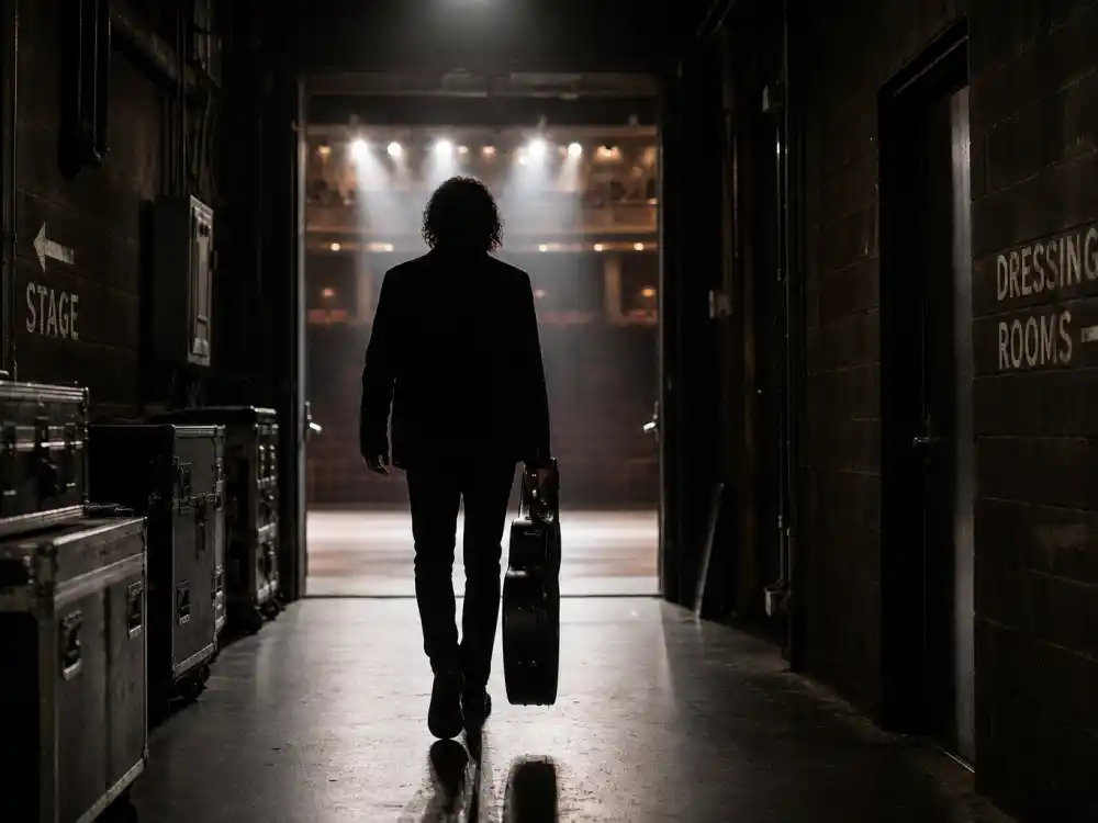 Musician silhouette walking away from a lit stage represents the sophomore slump behind the Best New Artist Grammy curse narrative