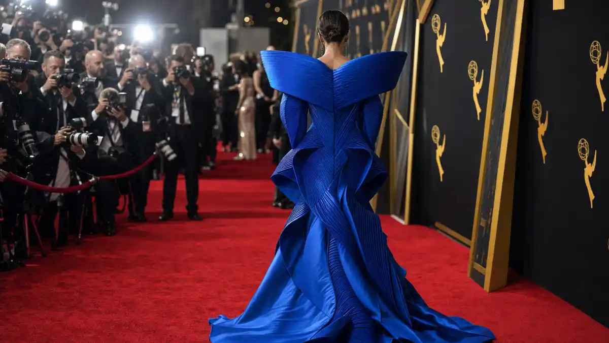 Biggest red carpet fashion risks that paid off — anonymous guest from behind in electric blue architectural shoulder gown on major awards red carpet with photographers and golden statuette backdrop