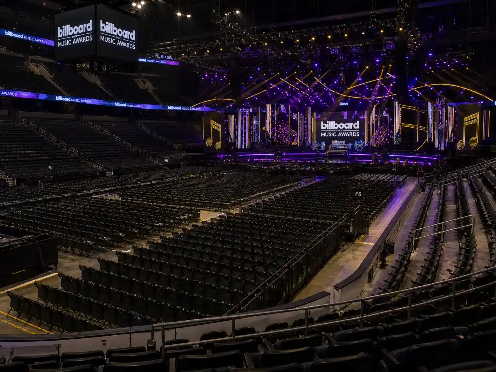 Concert arena interior before a Billboard Music Awards 2026 winners ceremony with purple and gold stage lighting rigs