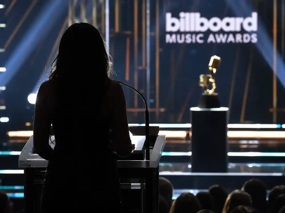 Anonymous presenter silhouette at a Billboard Music Awards 2026 winners predecessor podium facing a golden trophy on stage