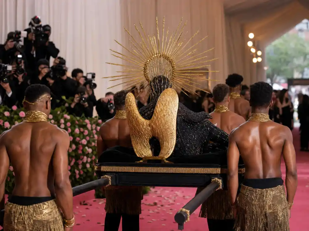 Theatrical litter palanquin entrance on Met Gala pink carpet amplifying Billy Porter sundial hat Met Gala camp performance and Sun God arrival