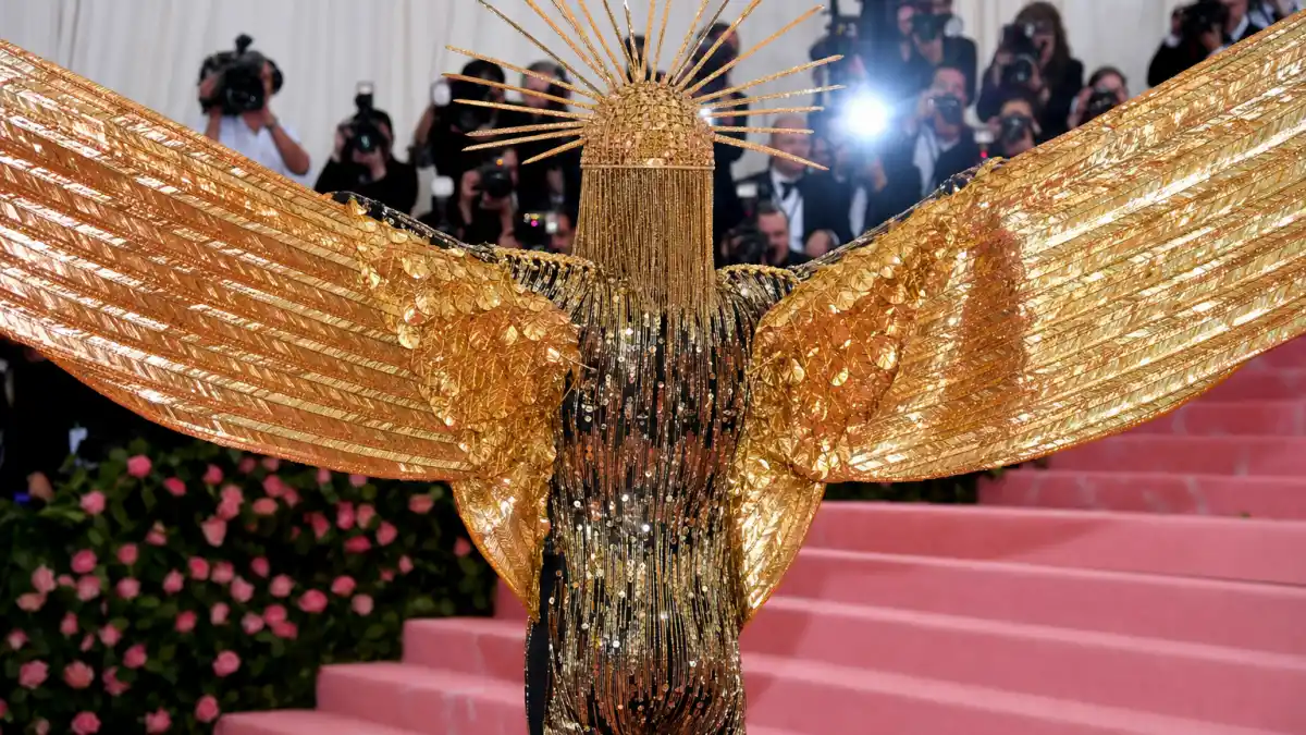 Billy Porter sundial hat Met Gala — gold Sun God headpiece with radiating rays and ten-foot wings photographed from behind on 2019 Camp Met Gala pink carpet