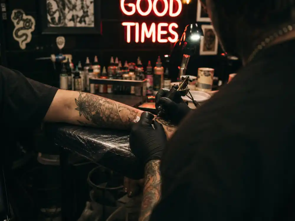 Tattoo parlor from behind artist shoulder for Brooklyn Beckham nepo baby ventures tattoo brand editorial without identifiable faces