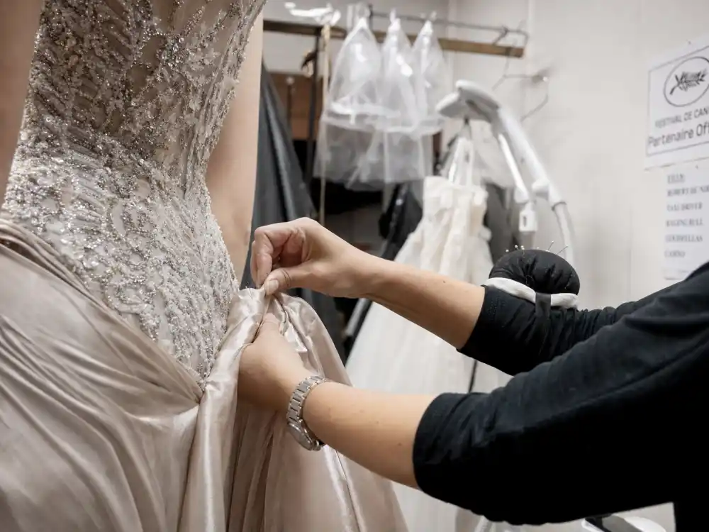 Stylist hands pinning silk train hem on couture gown bodice showing atelier craftsmanship behind cannes film festival celebrity style 2026 backstage fittings