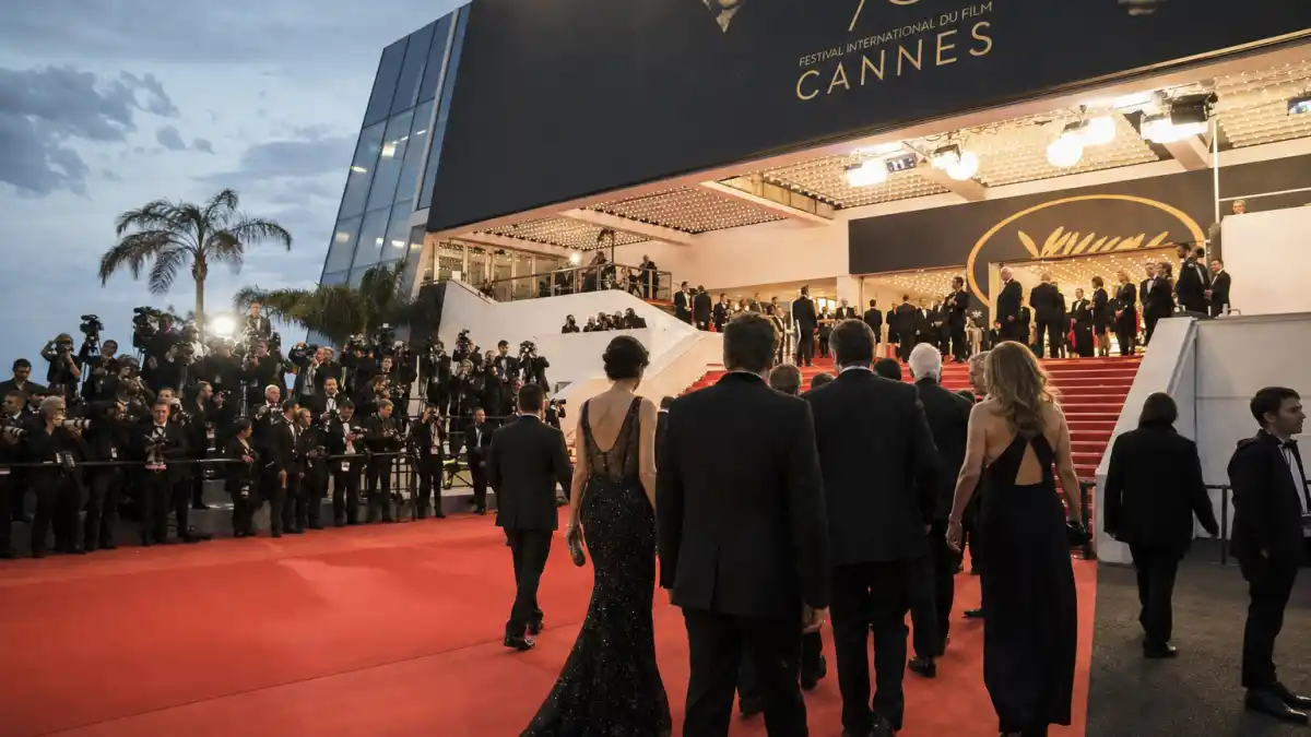 Cannes red carpet rules and dress code — formal black-tie guests climbing festival steps with photographers on risers at Palais des Festivals
