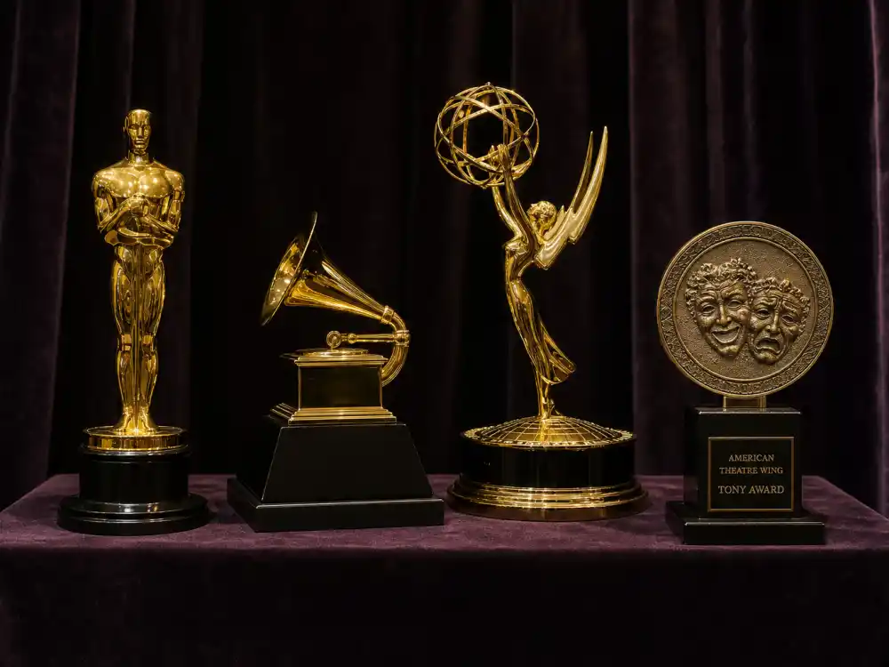 Museum row of four award statuettes illustrating celebrities close to an EGOT one trophy away from quadruple crown status