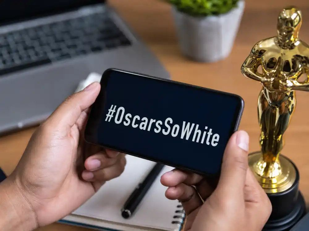 Smartphone showing OscarsSoWhite hashtag beside golden statuette illustrates social-media era celebrities who criticized the Oscars nomination slates