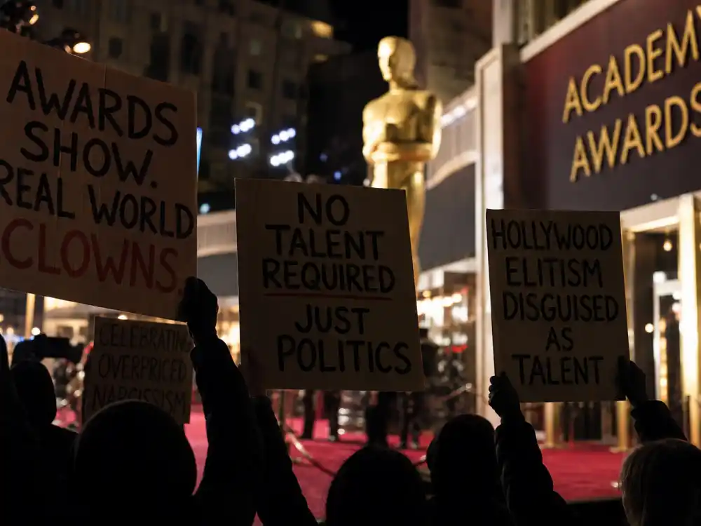 Anonymous hands holding protest signs outside a red carpet venue capture public anger behind celebrities who criticized the Oscars over diversity and institutional bias