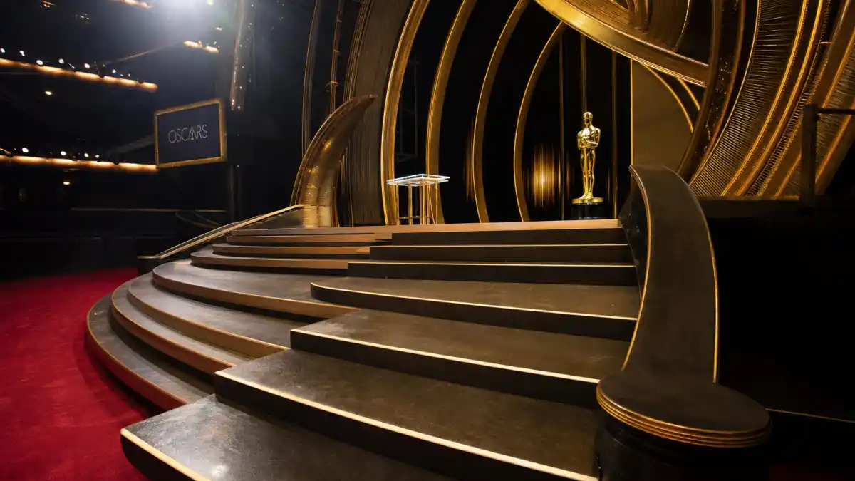 Celebrities who fell on stage at award shows — empty Oscars staircase with dramatic spotlight capturing the climb where famous stage trips happen