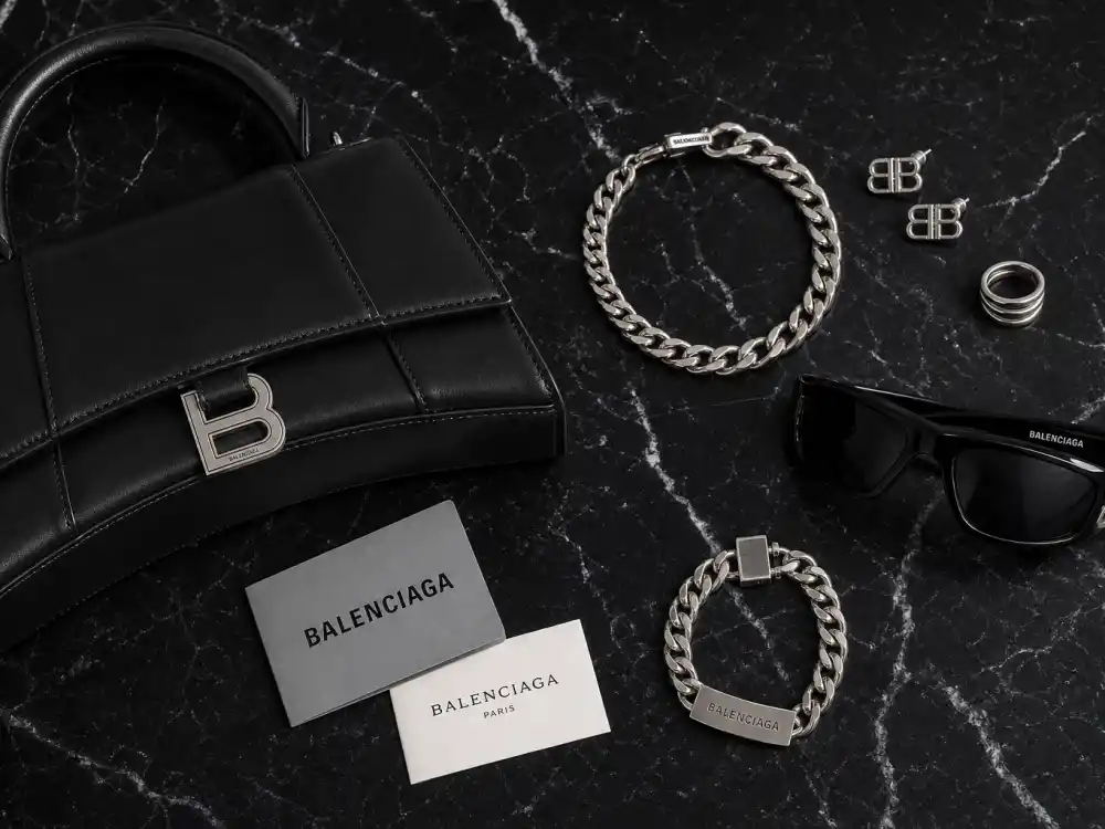 Balenciaga Hourglass handbag wrap sunglasses and chunky jewelry flat lay capturing accessory stacking rules celebrities who wear Balenciaga layer with oversized tailoring