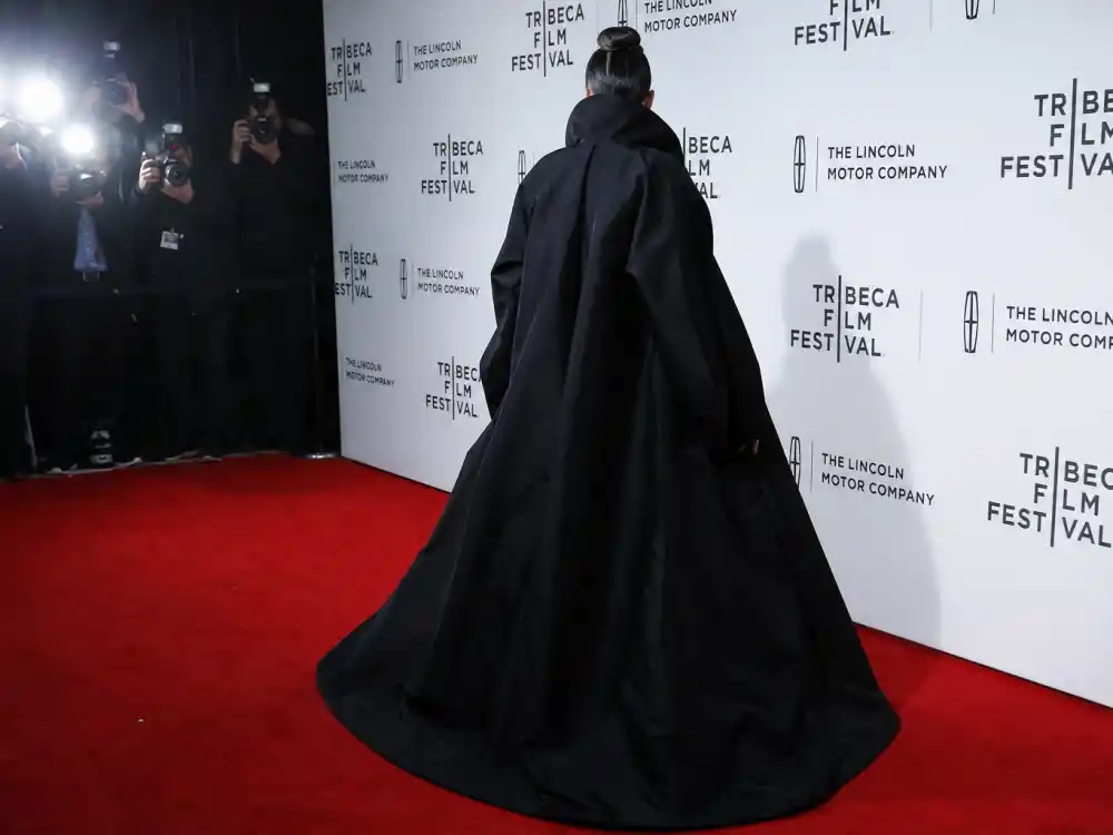 Anonymous woman in oversized black avant-garde coat photographed from behind at step-and-repeat showing how celebrities who wear Balenciaga command red carpet flash