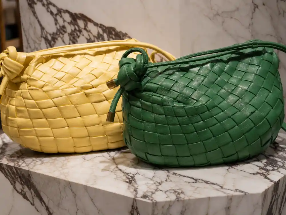 Bottega Veneta intrecciato woven leather handbags in signature green and tan on marble display defining the weave celebrities who wear Bottega Veneta pair with red carpet gowns and paparazzi looks
