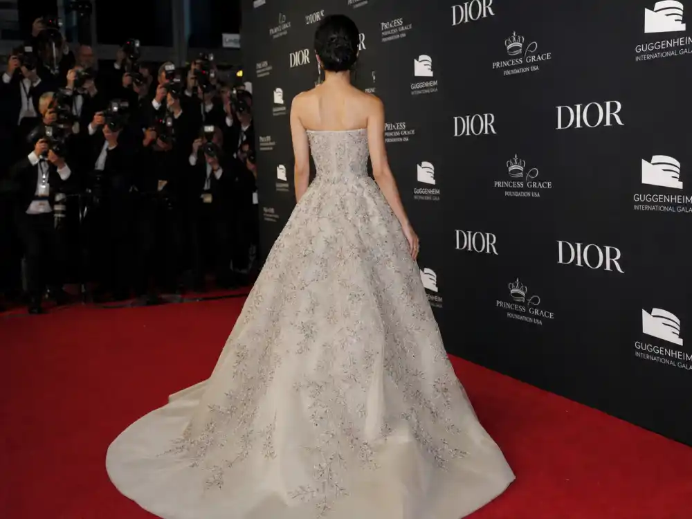 Anonymous woman in haute couture Dior evening gown photographed from behind at step-and-repeat showing how celebrities who wear Dior command red carpet visibility