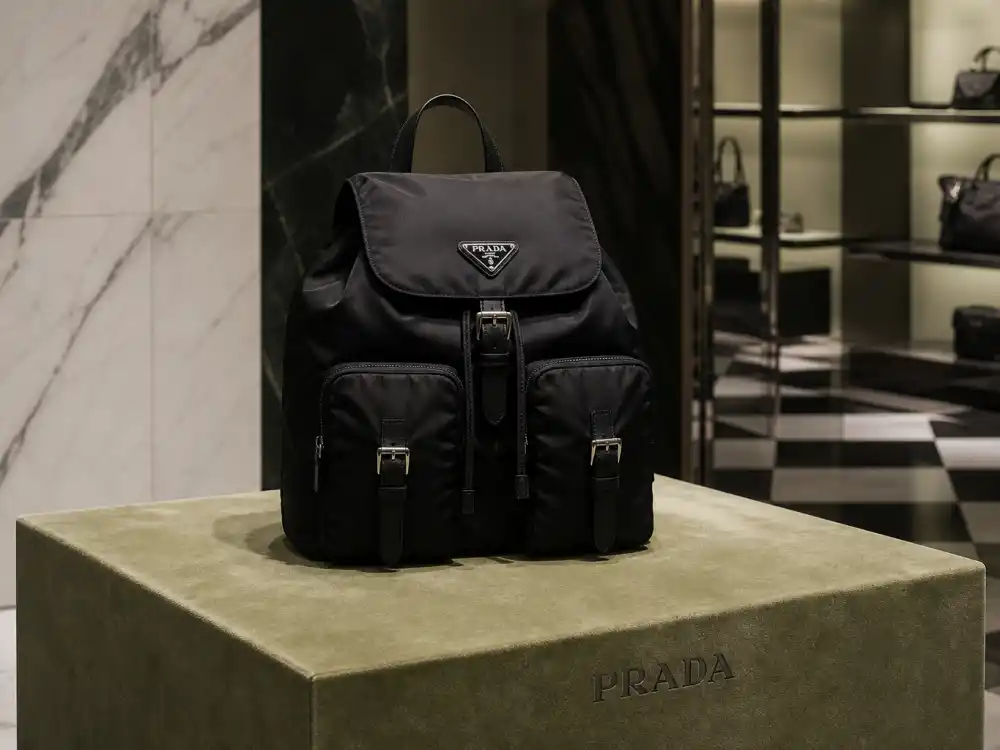 Iconic black Prada Re-Nylon backpack with triangle logo plaque defining the accessory code celebrities who wear Prada carry to paparazzi outings and fashion week circuits