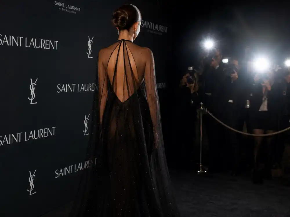 Anonymous woman in sheer black Saint Laurent evening gown photographed from behind at step-and-repeat showing how celebrities who wear Saint Laurent command red carpet visibility