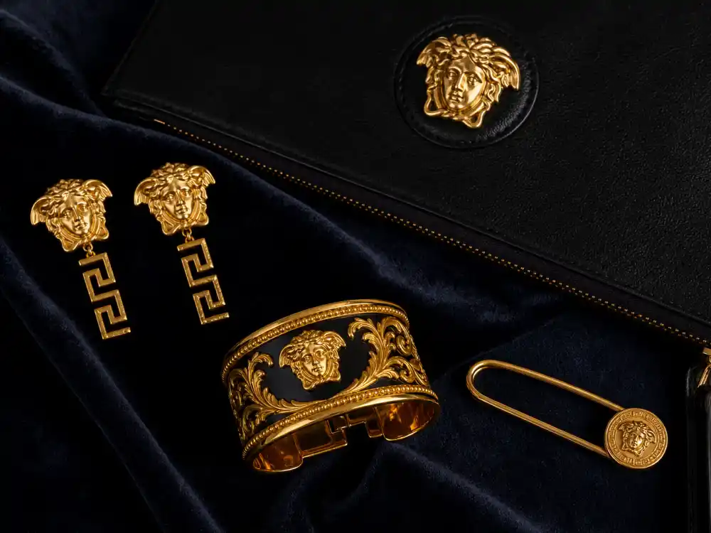 Gold Medusa earrings baroque cuff and safety pin brooch flat lay capturing accessory stacking rules celebrities who wear Versace use when gowns alone cannot carry camera