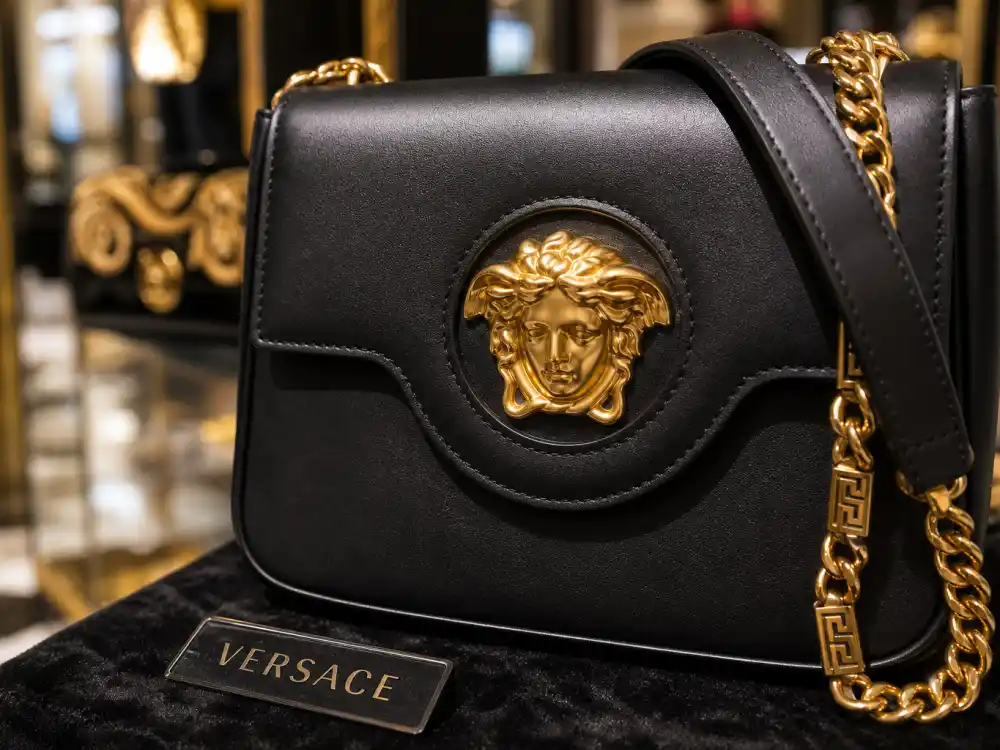 Gold Medusa head logo on black Versace handbag with baroque chain strap defining the accessory code celebrities who wear Versace carry to premieres and paparazzi outings