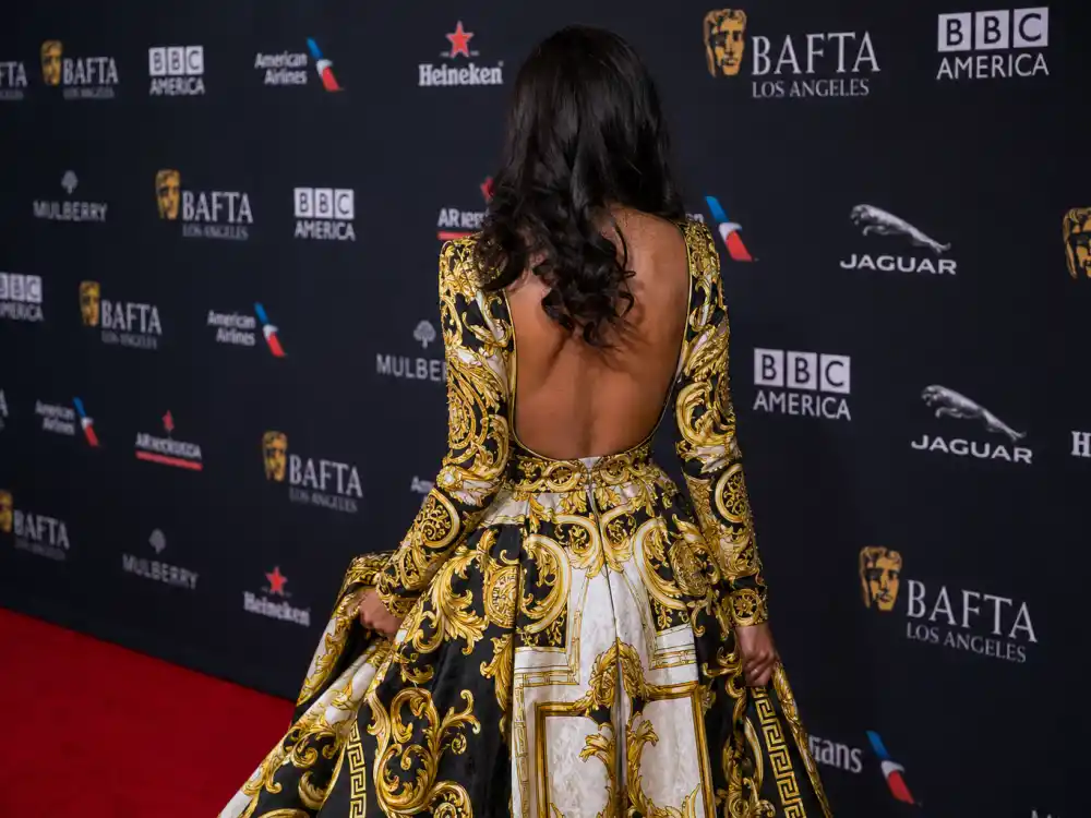 Anonymous woman in bold Versace baroque print gown photographed from behind at step-and-repeat showing how celebrities who wear Versace command red carpet visibility