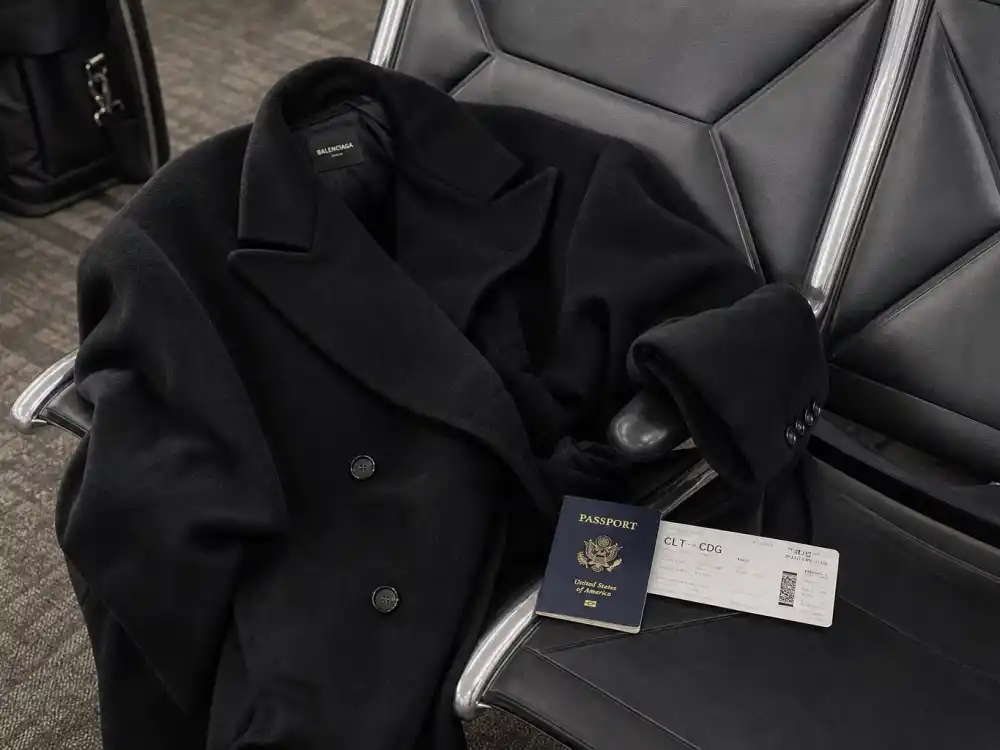 Oversized black wool coat on airport lounge chair central to celebrity airport fashion street style outerwear codes
