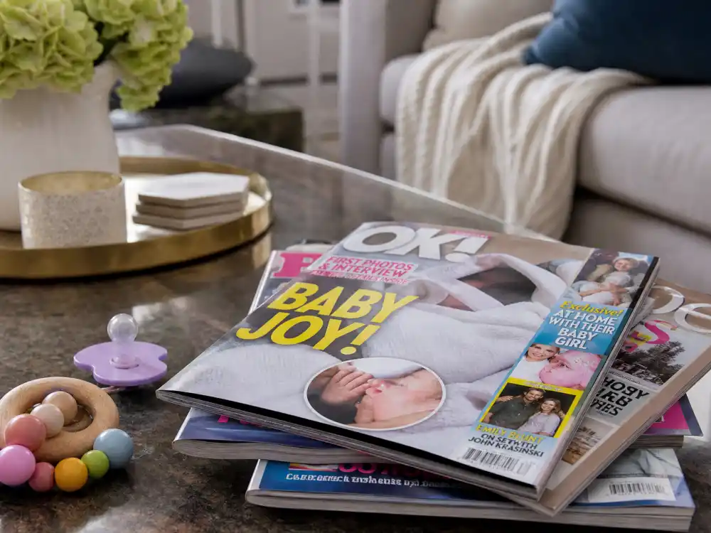 Magazine stack and baby rattle on coffee table — celebrity babies born in 2026 dominate the entertainment news cycle