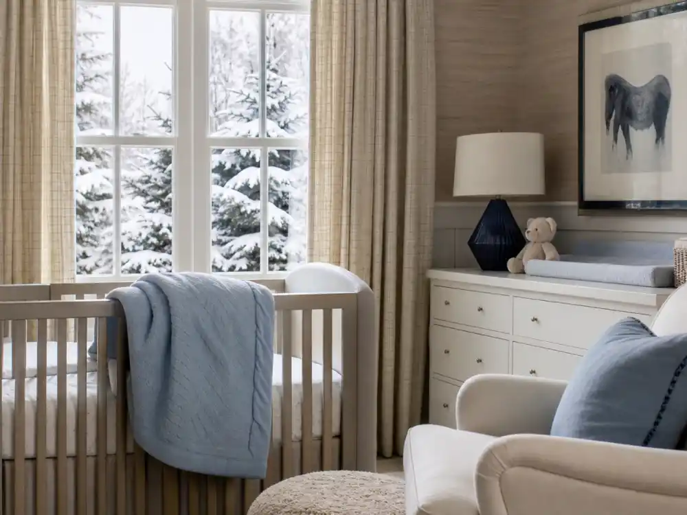 Winter nursery scene for celebrity babies born in 2026 — cozy crib with blue blanket and snow visible through the window