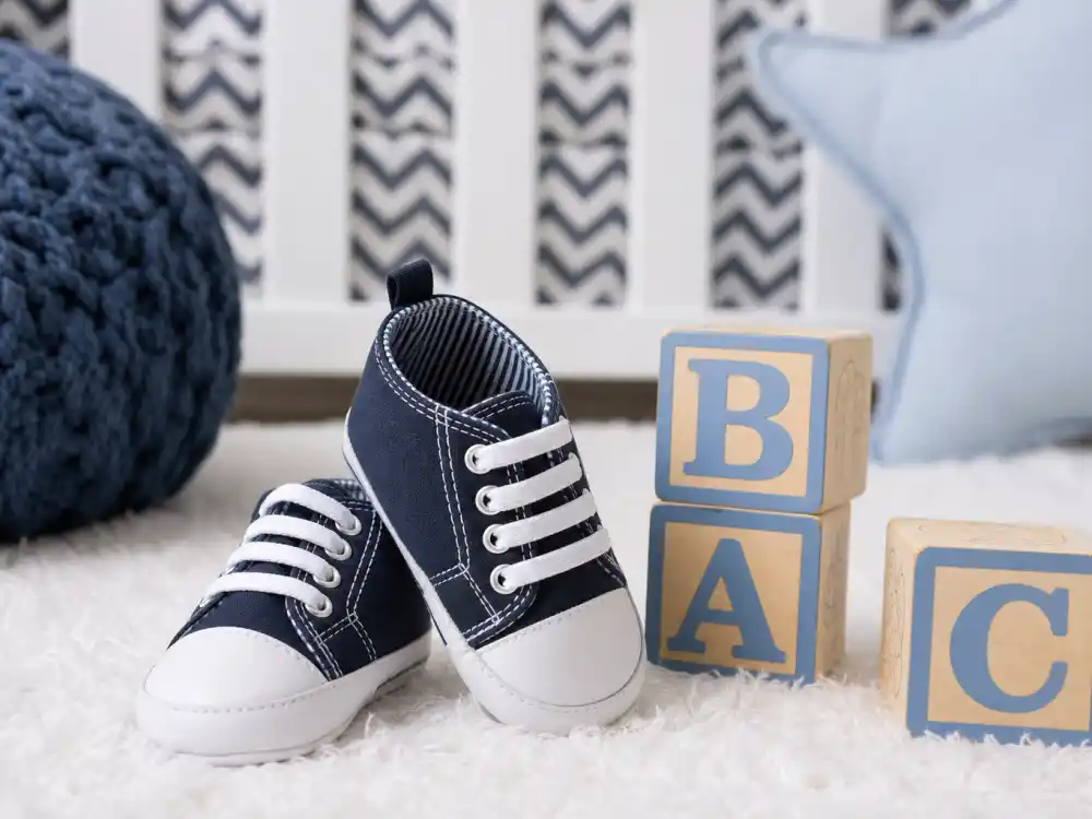Tiny navy blue baby boy sneakers on white nursery rug beside wooden alphabet blocks — celebrity baby boy names inspired by stars decode culture starts with confirmed spellings