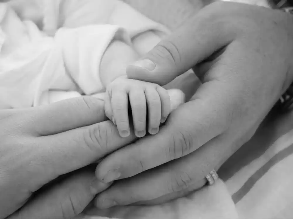 Black-and-white hand-grasp photo for celebrity birth announcements Instagram 2026 — parent fingers curled around newborn without showing faces