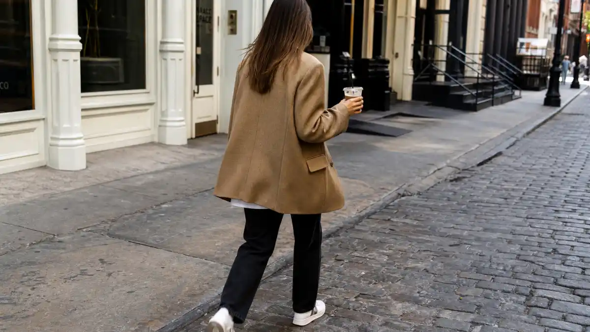 Celebrity blazer street style outfits — camel oversized blazer white tee black jeans white sneakers on SoHo cobblestone sidewalk seen from behind
