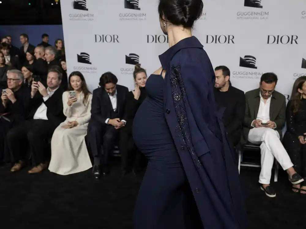 Pregnant woman in navy couture coat at luxury step-and-repeat for celebrity bump style red carpet front-row event coverage