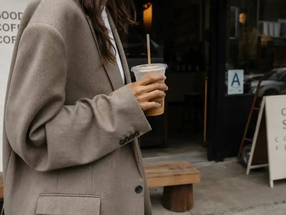 Iced coffee to-go cup in hand with oversized blazer sleeve illustrating celebrity coffee run outfits street style morning ritual