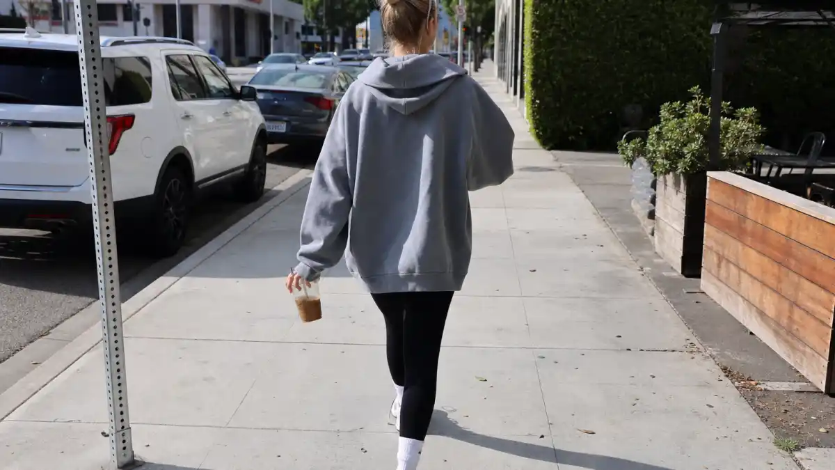 Celebrity coffee run outfits street style — oversized gray hoodie black leggings white sneakers and iced coffee on LA sidewalk seen from behind