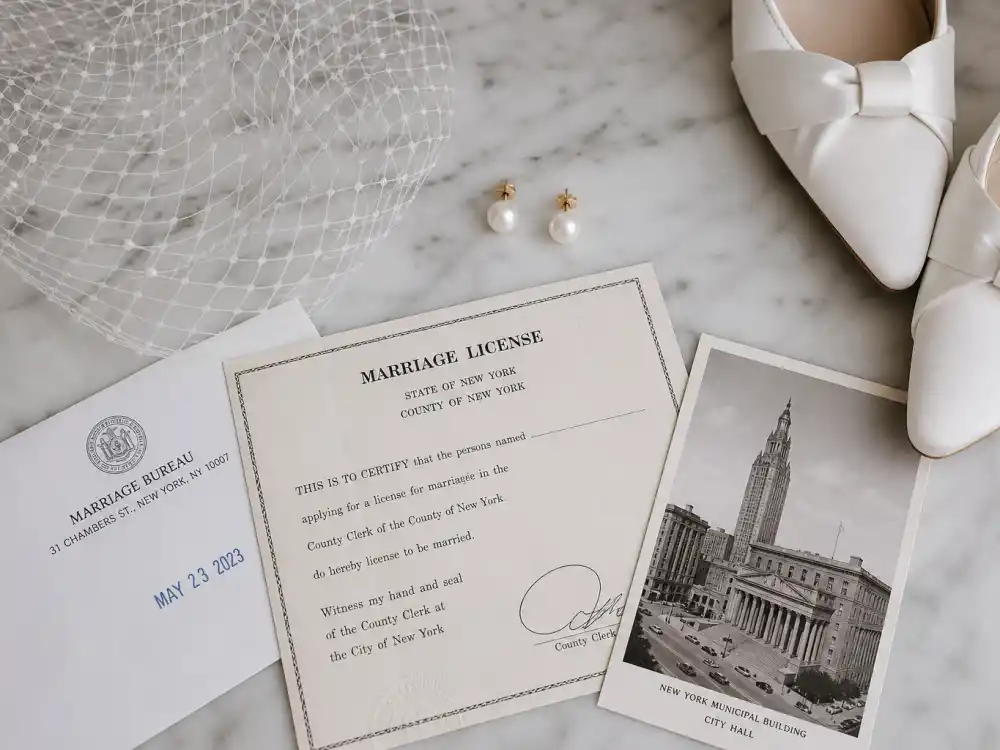 Pearl earrings fingertip veil and marriage paperwork accessories completing celebrity courthouse wedding outfits flat lay on marble