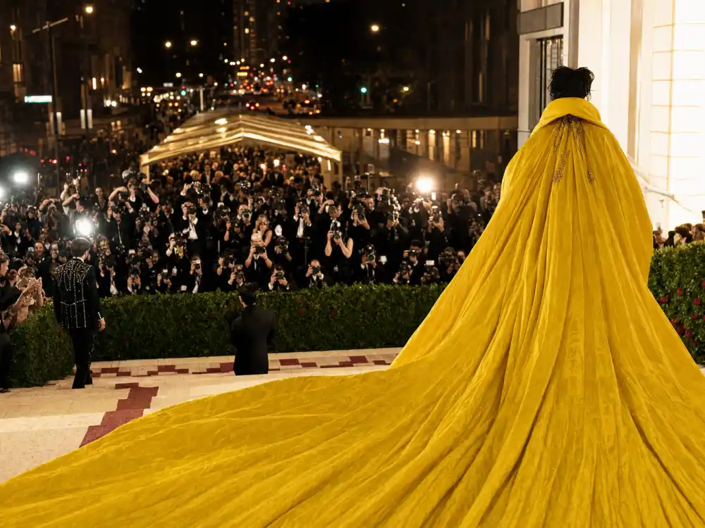 Anonymous figure from behind on gala museum steps in dramatic yellow couture cape with photographers below capturing celebrity fashion moments that broke the internet