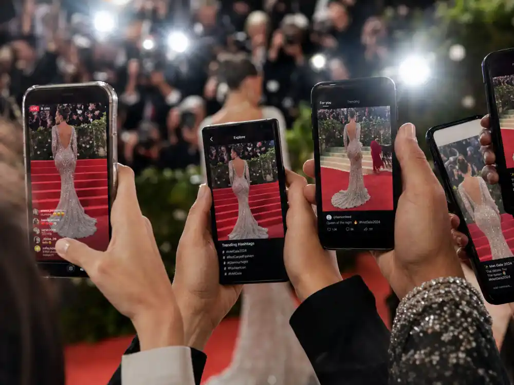 Smartphones in a red carpet crowd showing social media feeds with viral celebrity fashion moments that broke the internet trending across platforms